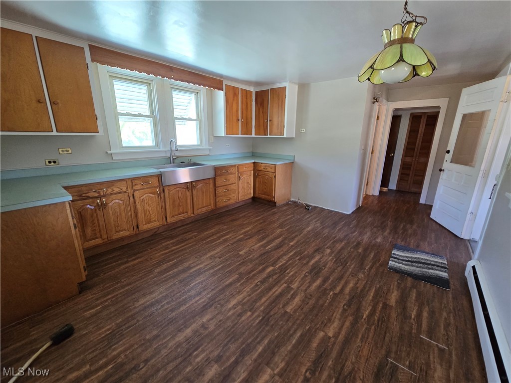 5555 Detroit Road Sheffield, OH 44054 - Photo 7 of 50 Kitchen featuring baseboard heating, dark wood-type flooring, light countertops, pendant lighting, and brown cabinets