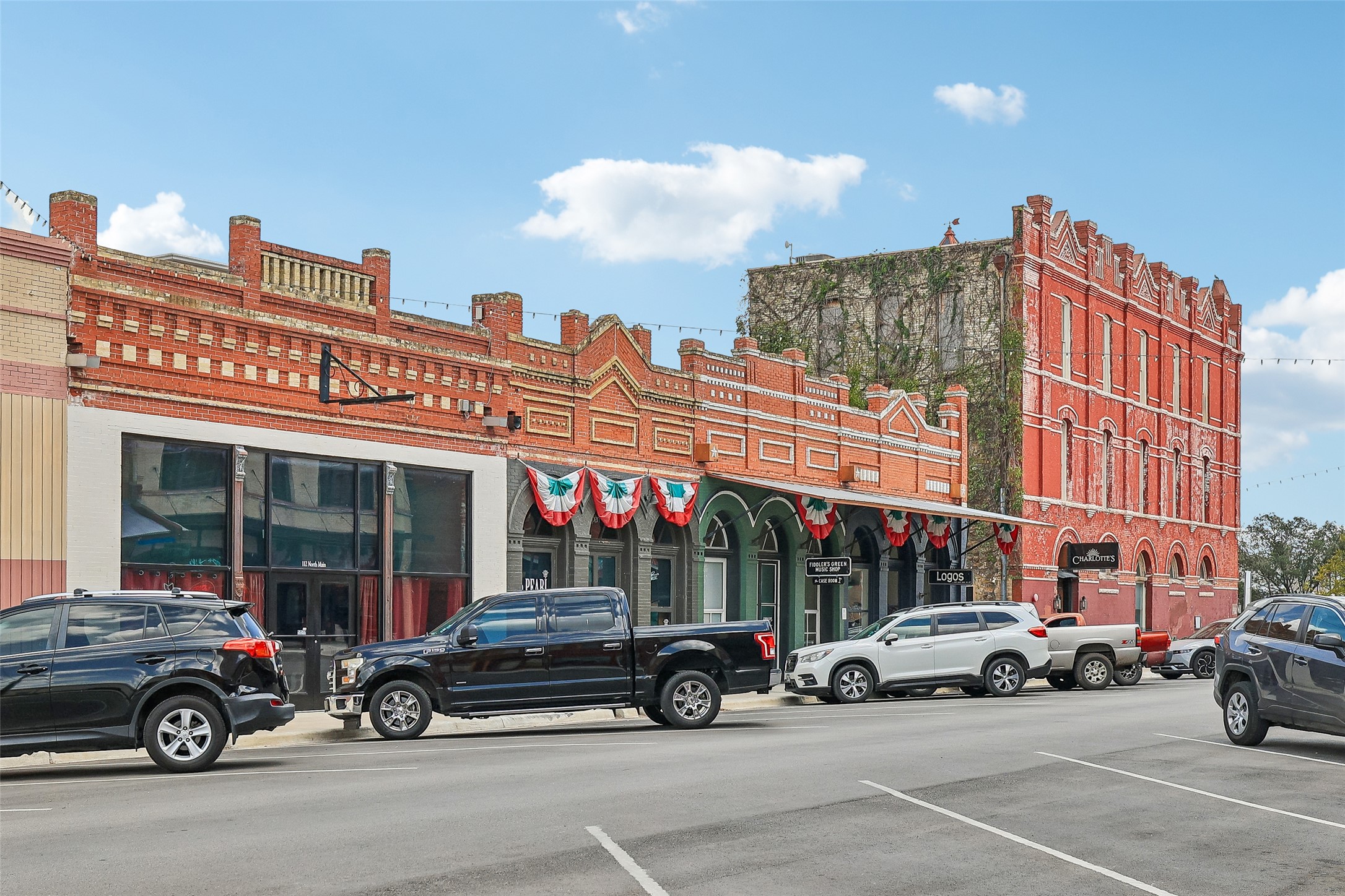 372 Old Lockhart Road Lockhart, TX 78644 - Photo 39 of 40 Historic brick storefronts anchor this vibrant streetscape under a bright blue sky.