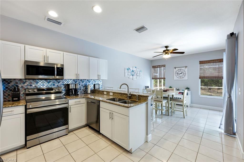 697 Crossfield Circle Naples, FL 34104 - Photo 8 of 18 Kitchen with appliances with stainless steel finishes, a peninsula, decorative backsplash, ceiling fan, and white cabinetry