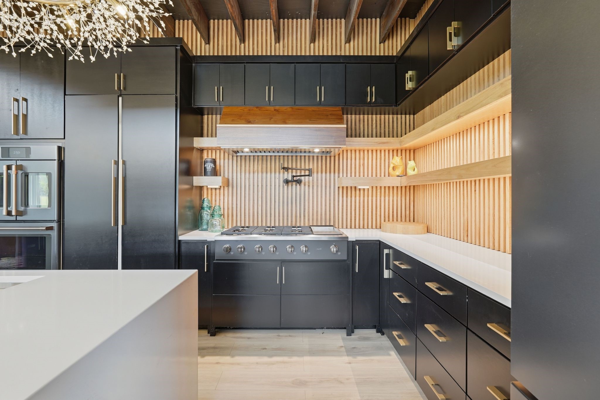 2743 Bobville Road Montgomery, TX 77316 - Photo 21 of 50 This modern kitchen features sleek black cabinetry with gold accents, a gas stove, and open shelving with wood accents. It includes a large refrigerator, built-in oven, and stylish lighting, creating a chic and functional space.