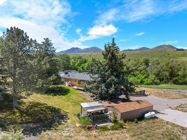 15680 North Beaver Dam Road Collinston, UT 84306 - Photo 47 of 49 Sprawling property featuring a single-story residence with a dark roof and light-colored siding, a wooden deck, and a lush green lawn