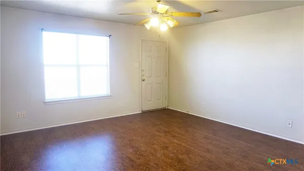 a view of an empty room with wooden floor and a window