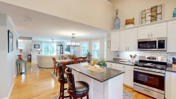 a open kitchen with stainless steel appliances kitchen island granite countertop a stove top oven a sink dishwasher and white cabinets with wooden floor