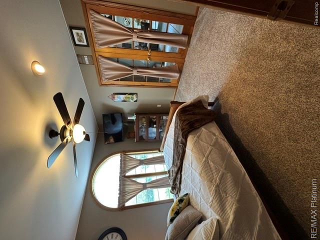 4457 Bradley Road Gregory, MI 48137 - Photo 79 of 79 Spacious primary bedroom suite featuring a ceiling fan with integrated lighting, arched transom windows with custom drapery hardware, mirrored sliding closet doors, neutral carpeting, and access to adjacent glass doors opening to outdoor space