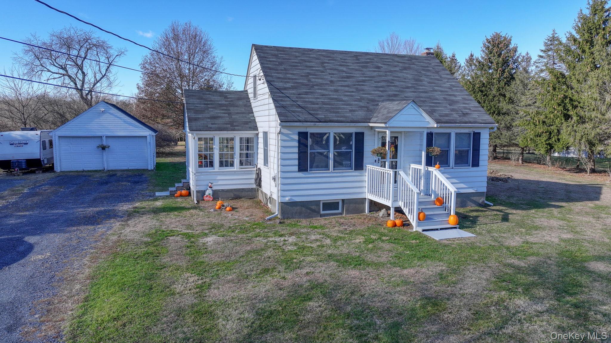 View of front facade featuring an outdoor structure, a detached garage, roof with shingles, and a front yard