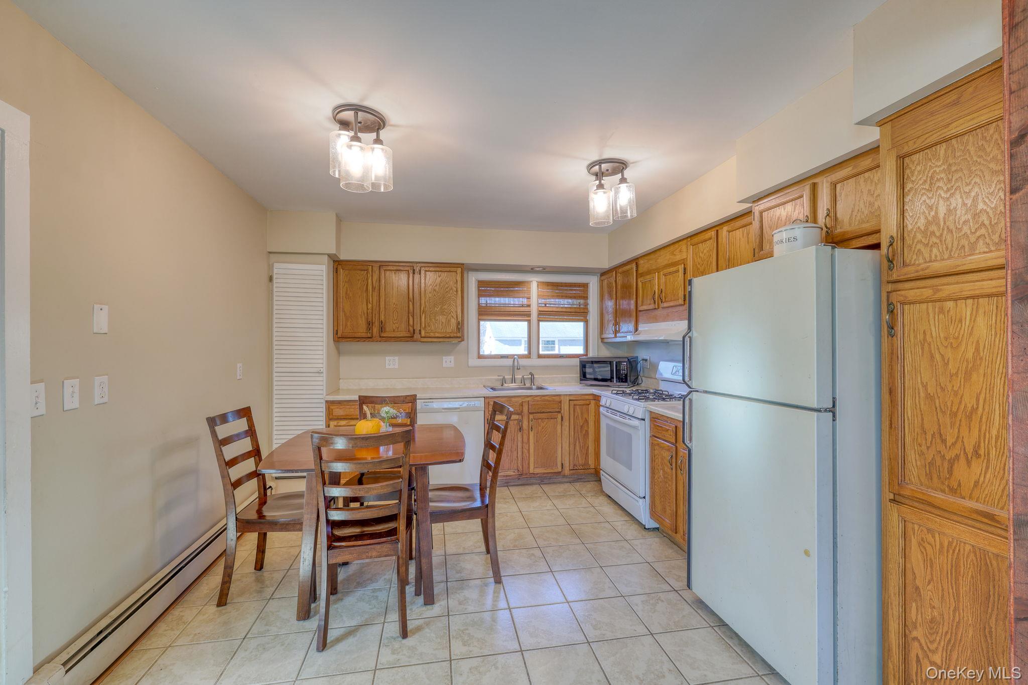 143 Plains Road Walden, NY 12586 - Photo 7 of 36 Kitchen featuring white appliances, light countertops, a baseboard radiator, light tile patterned floors, and brown cabinets