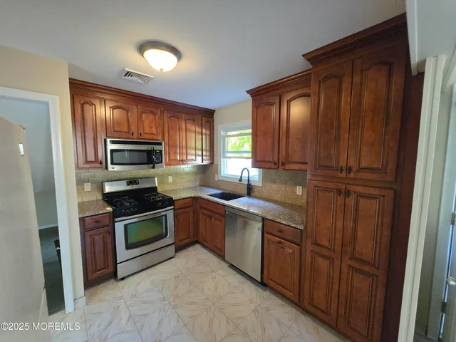 a kitchen with stainless steel appliances granite countertop wooden cabinets a stove top oven a sink and dishwasher