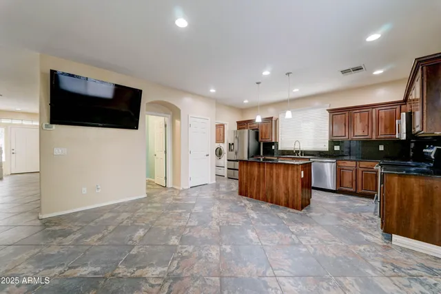 a view of kitchen with stainless steel appliances kitchen island granite countertop a refrigerator and a view of living room