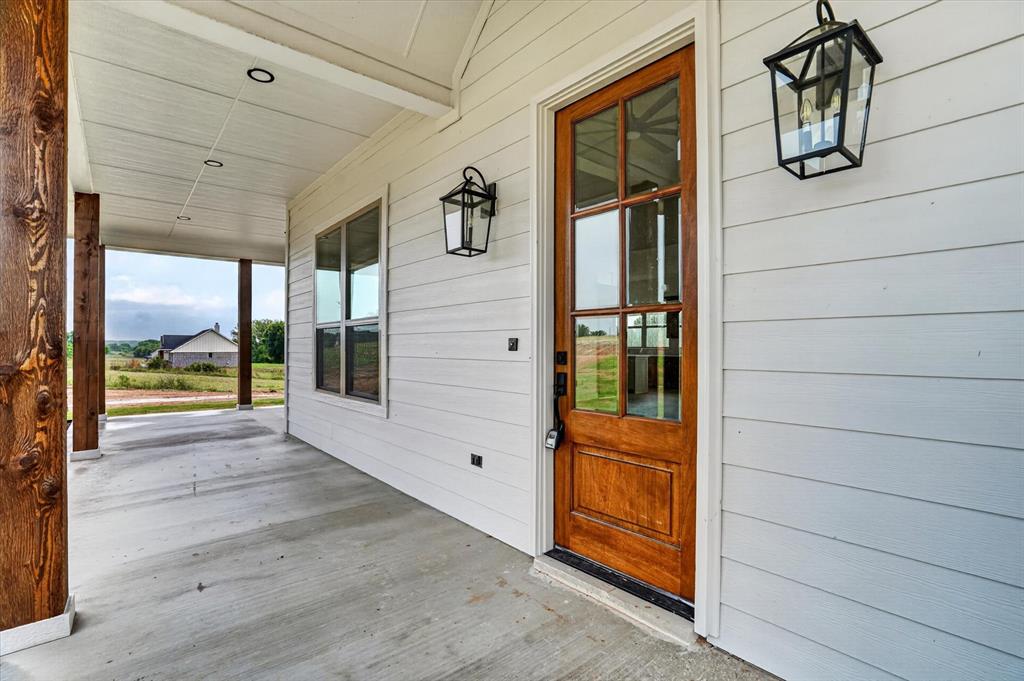 225 Kilkenny Road Poolville, TX 76487 - Photo 4 of 36 Inviting front porch featuring a wood-panel entry door with glass inserts, white horizontal siding, and rustic wood posts