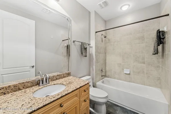 a bathroom with a granite countertop bathtub shower sink vanity mirror and toilet