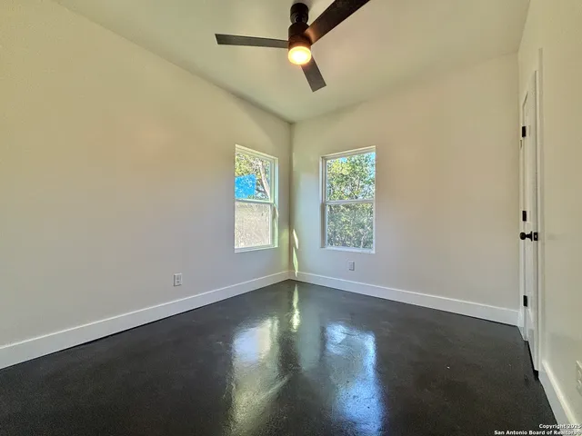 an empty room with wooden floor chandelier fan and windows