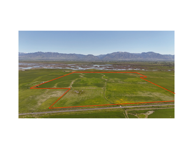 Expansive agricultural land featuring a verdant field, visible waterways, and distant mountain ranges