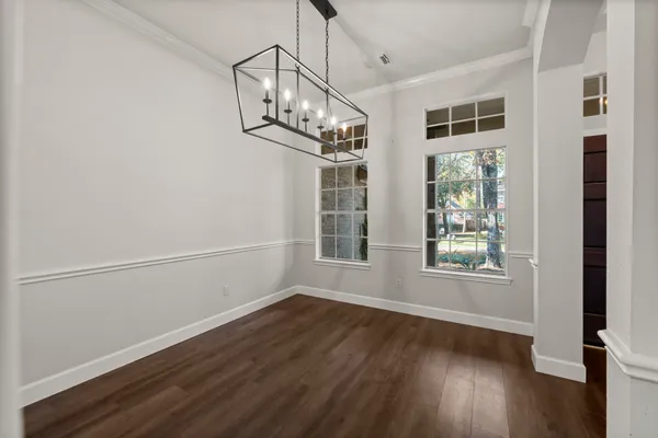 an empty room with wooden floor chandelier and windows