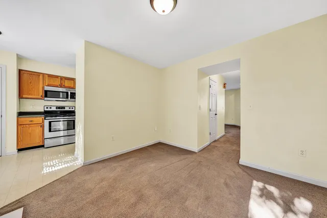 a view of an empty room with kitchen and a window