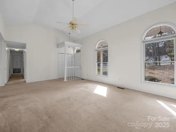 an empty room with chandelier fan and windows