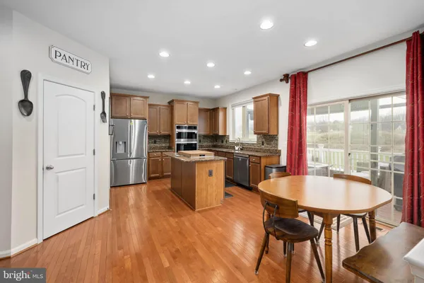 a kitchen with stainless steel appliances granite countertop a stove top oven a sink a dining table and chairs with wooden floor