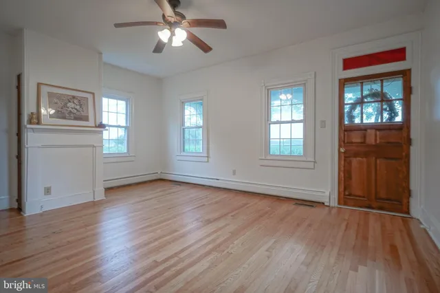 an empty room with wooden floor chandelier fan and windows