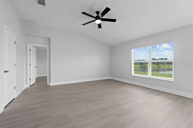 an empty room with wooden floor a ceiling fan and windows