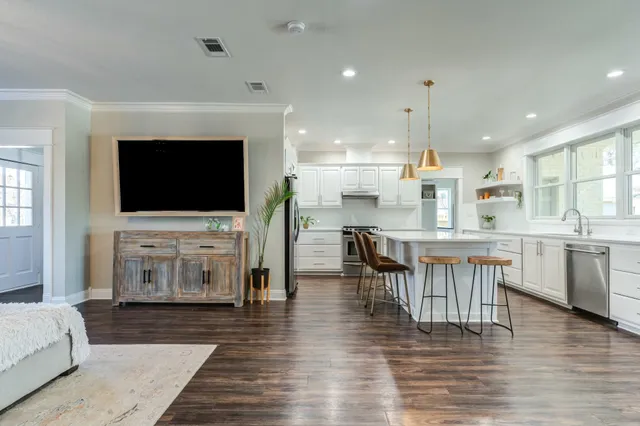 a living room with stainless steel appliances furniture a flat screen tv and kitchen view