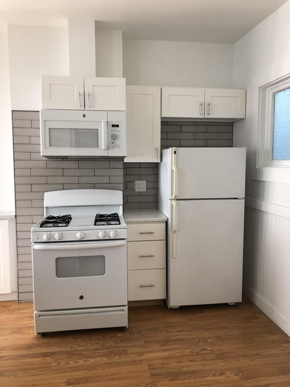 a white refrigerator freezer and a stove sitting inside of a kitchen with granite countertop white cabinets