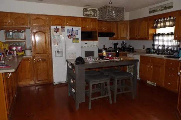 a kitchen with stainless steel appliances granite countertop a refrigerator a sink dishwasher a stove a dining table and chairs with wooden floor