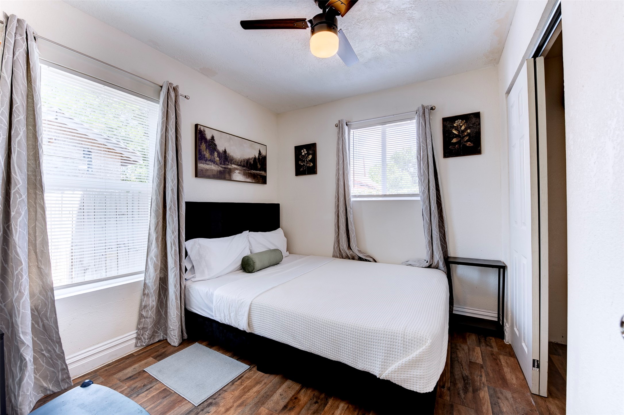 1121 Panama Street Houston, TX 77009 - Photo 23 of 35 Bedroom featuring dark wood-look LVP flooring, ceiling fan with light kit, dual windows with blinds and grommet curtains, and a reach-in closet with sliding door.