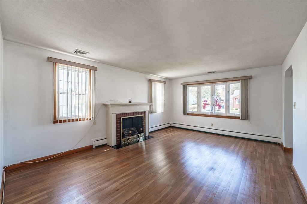 127 Cheyenne Road Springfield, MA 01109 - Photo 7 of 42 an empty room with windows fireplace and wooden floor