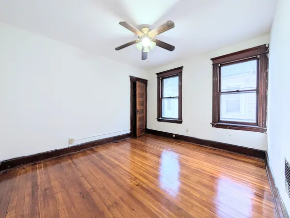 an empty room with wooden floor chandelier fan and windows