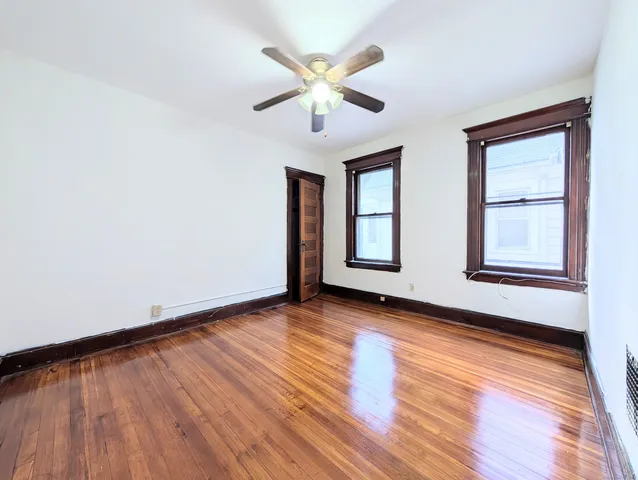 an empty room with wooden floor chandelier fan and windows