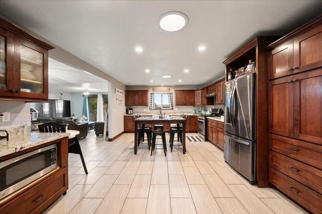 a kitchen with stainless steel appliances kitchen island granite countertop a refrigerator a stove a dining table and chairs with wooden floor