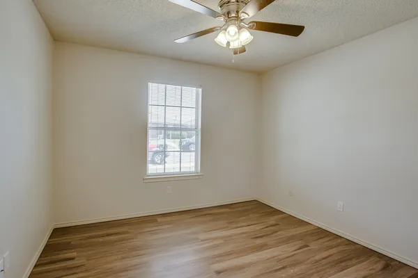 an empty room with wooden floor chandelier fan and windows