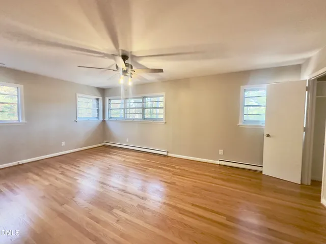 an empty room with wooden floor fan and windows