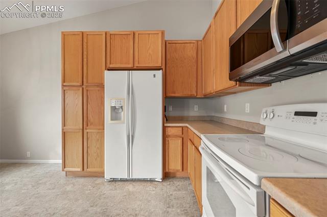 11927 Rodez Grove Peyton, CO 80831 - Photo 13 of 34 Kitchen featuring lofted ceiling, light countertops, white appliances, and baseboards