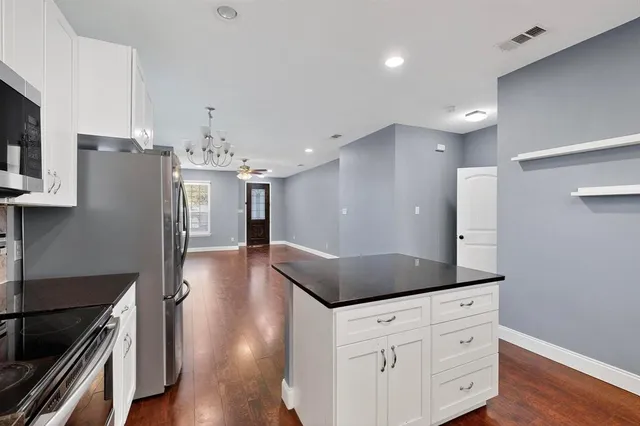 a kitchen with stainless steel appliances kitchen island granite countertop a refrigerator a stove and a wooden floors