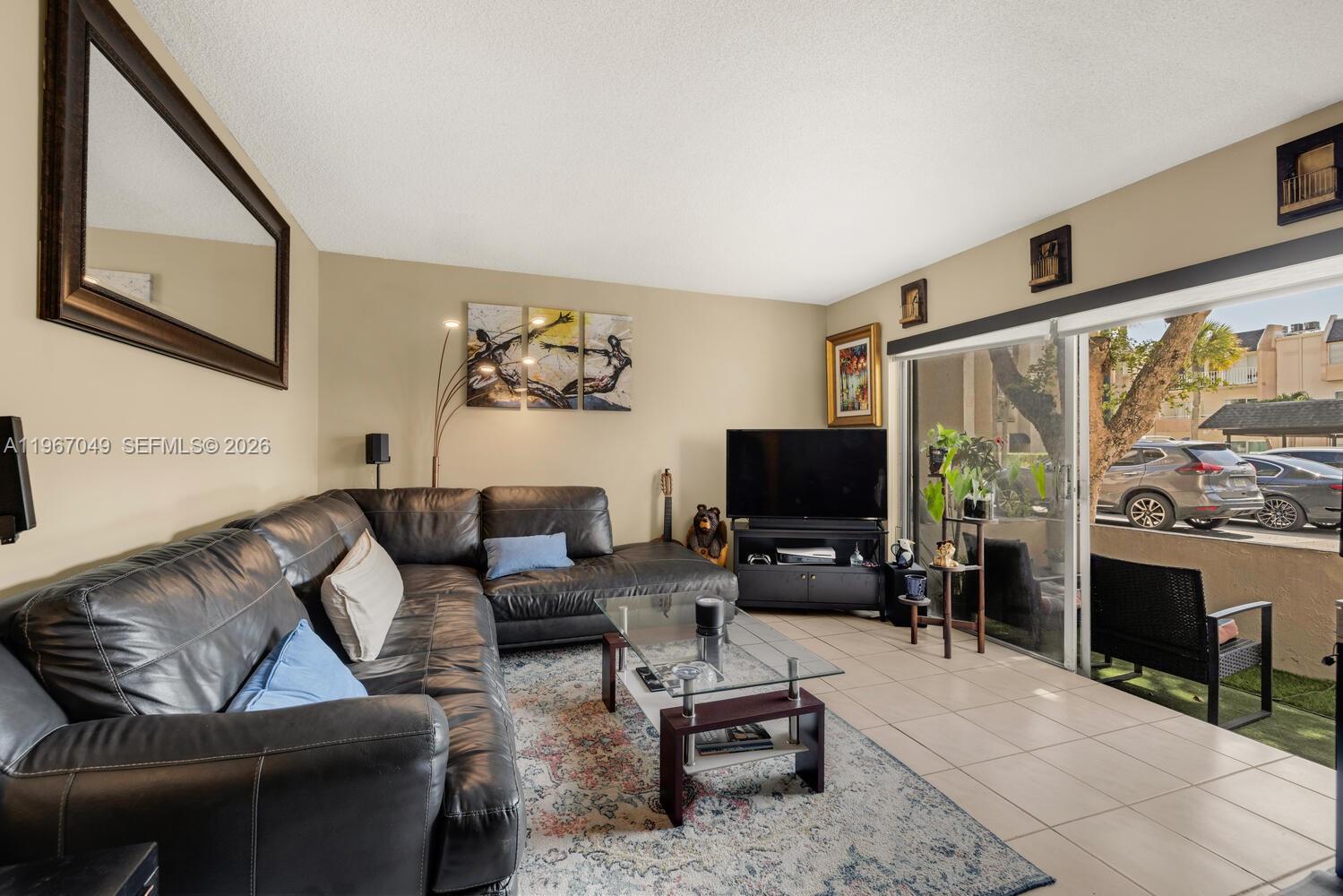 7785 Southwest 86th Street, Unit E119 Miami, FL 33143 - Photo 6 of 33 a living room with furniture a flat screen tv and a floor to ceiling window