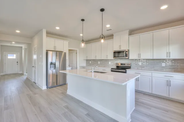 a kitchen with stainless steel appliances granite countertop a refrigerator a sink dishwasher a stove and white cabinets with wooden floor