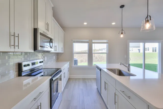 a kitchen with stainless steel appliances a sink a stove a refrigerator white cabinets and wooden floor