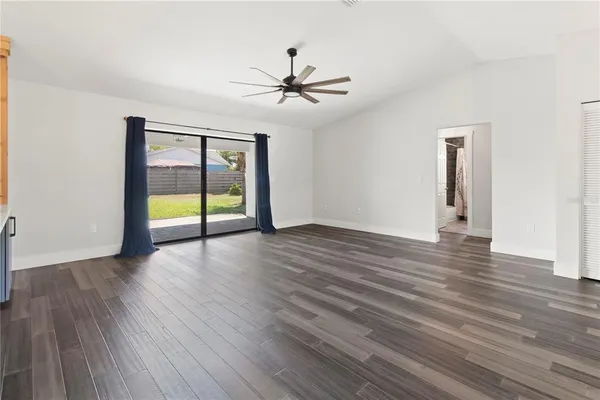 an empty room with wooden floor chandelier fan and windows