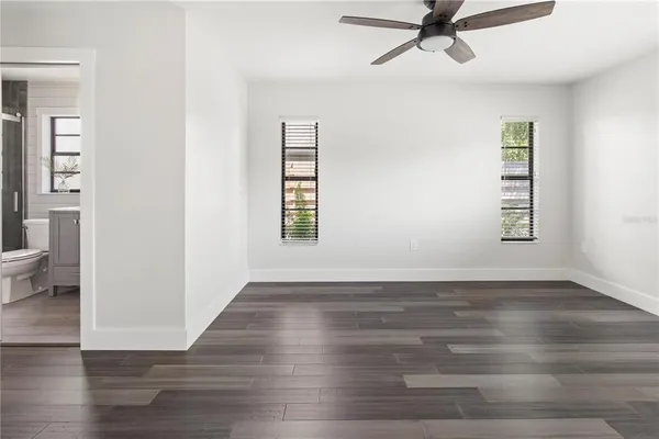 an empty room with wooden floor a ceiling fan and windows