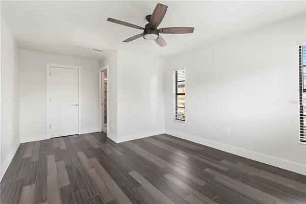 an empty room with wooden floor ceiling fan and windows