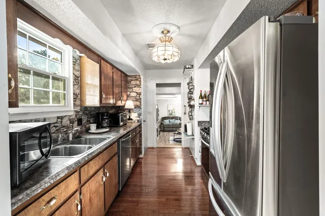 a kitchen with granite countertop a refrigerator a sink dishwasher a stove and a dining table next to a window