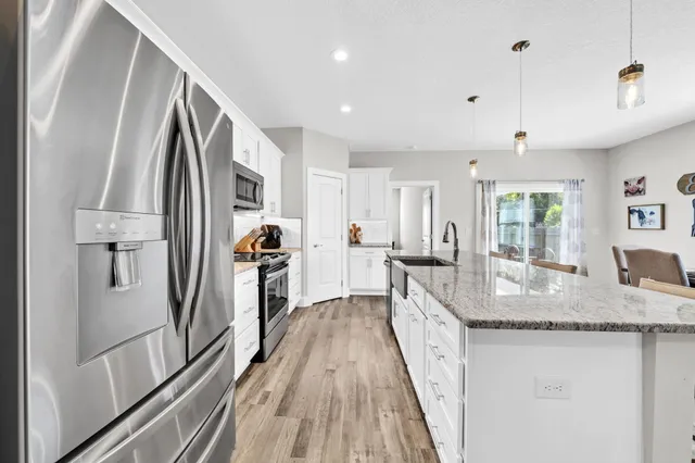 a kitchen with granite countertop a refrigerator a sink dishwasher a stove and white countertops with wooden floor