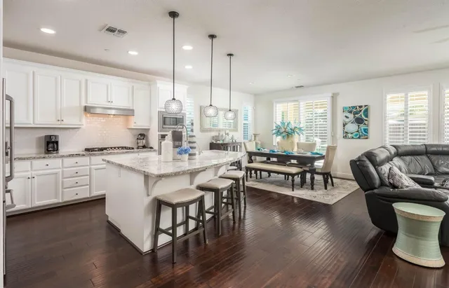 a kitchen with stainless steel appliances granite countertop a stove a refrigerator a kitchen island a sink and a wooden floor