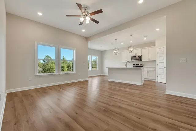 an empty room with wooden floor kitchen view and a window