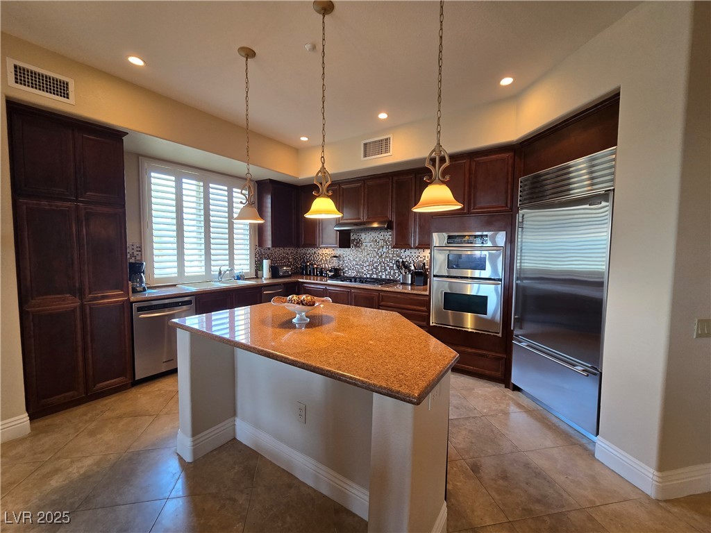 20 Via Mantova, Unit 202 Henderson, NV 89011 - Photo 15 of 60 Kitchen with stainless steel appliances, a kitchen island, tasteful backsplash, pendant lighting, and light stone countertops