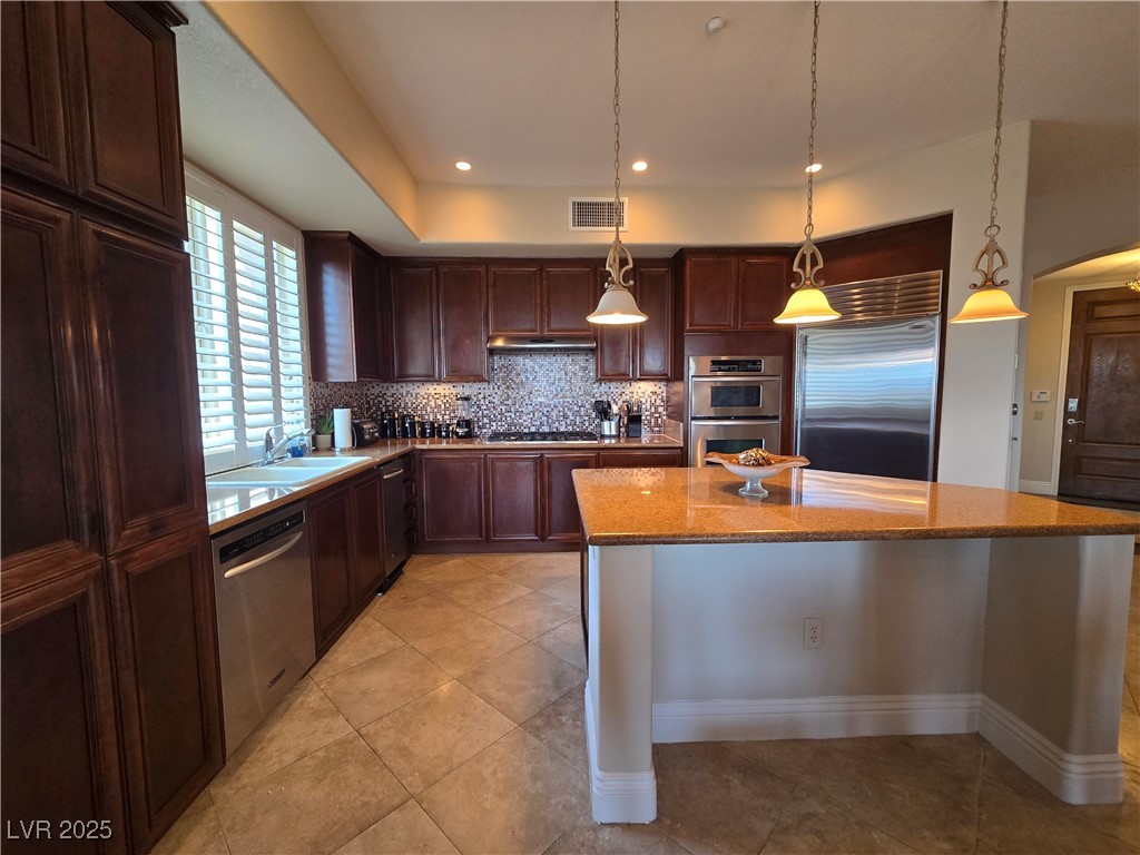 20 Via Mantova, Unit 202 Henderson, NV 89011 - Photo 16 of 60 Kitchen featuring stainless steel appliances, decorative backsplash, a kitchen island, light stone countertops, and light tile patterned floors