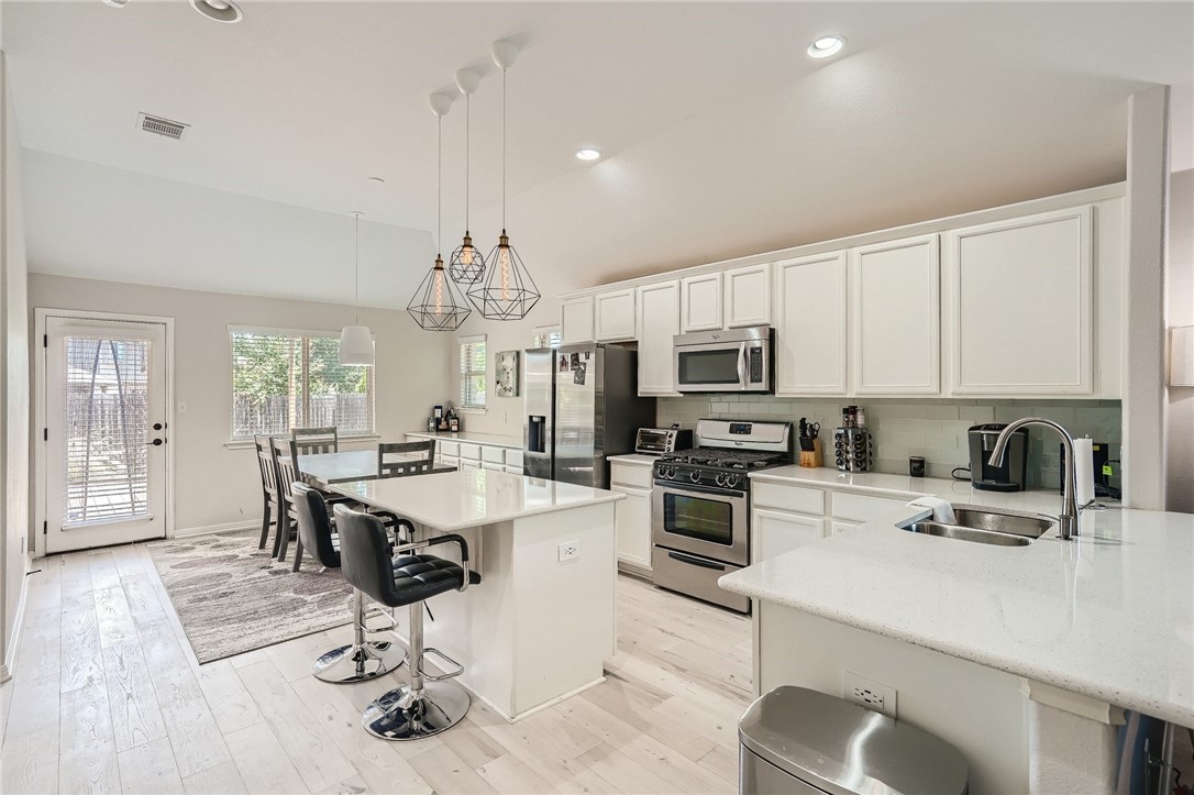 7108 Hester Road Austin, TX 78725 - Photo 4 of 25 a kitchen with kitchen island granite countertop a stove a sink a oven a dining table and chairs with wooden floor
