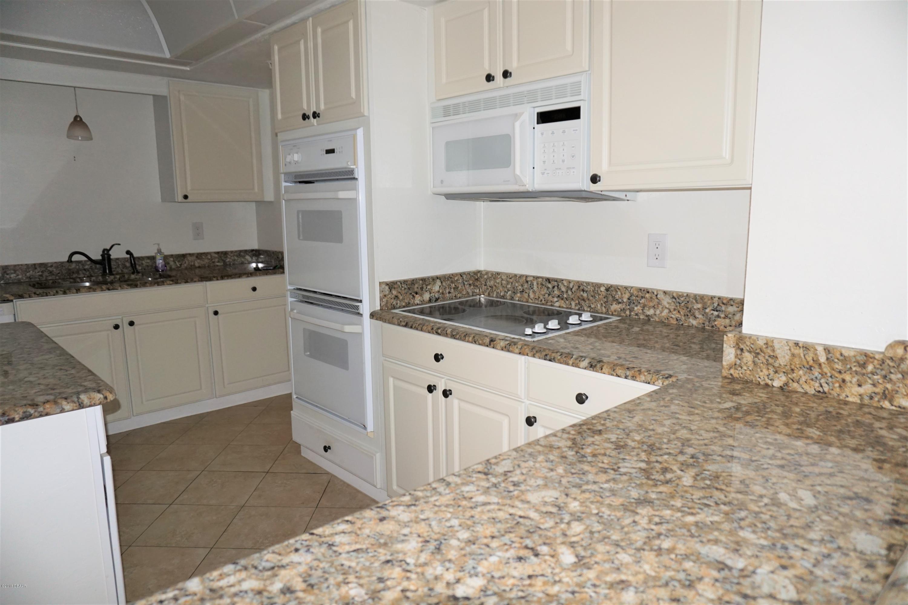 1 John Anderson Drive, Unit 113 Ormond Beach, FL 32176 - Photo 15 of 76 a kitchen with granite countertop white cabinets and white appliances