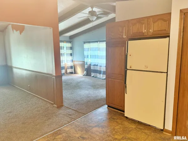 a view of a refrigerator in kitchen and an empty room