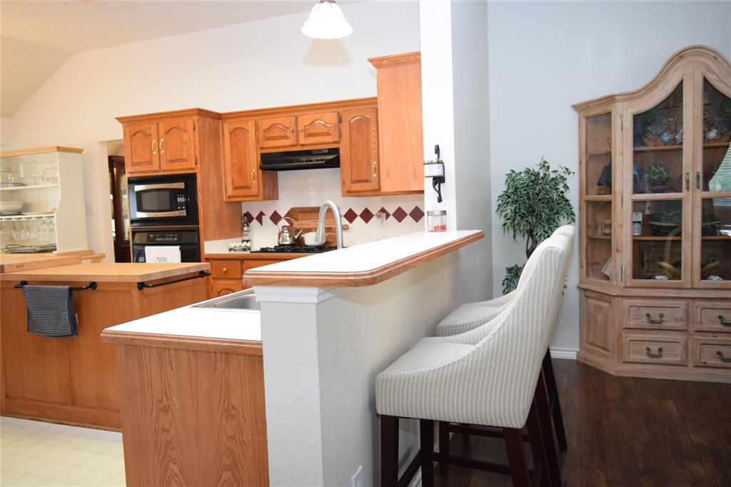 4201 Glistening Spring Rowlett, TX 75088 - Photo 6 of 33 Kitchen featuring wood-finish cabinetry, built-in microwave, integrated oven, and a breakfast bar with solid surface countertop